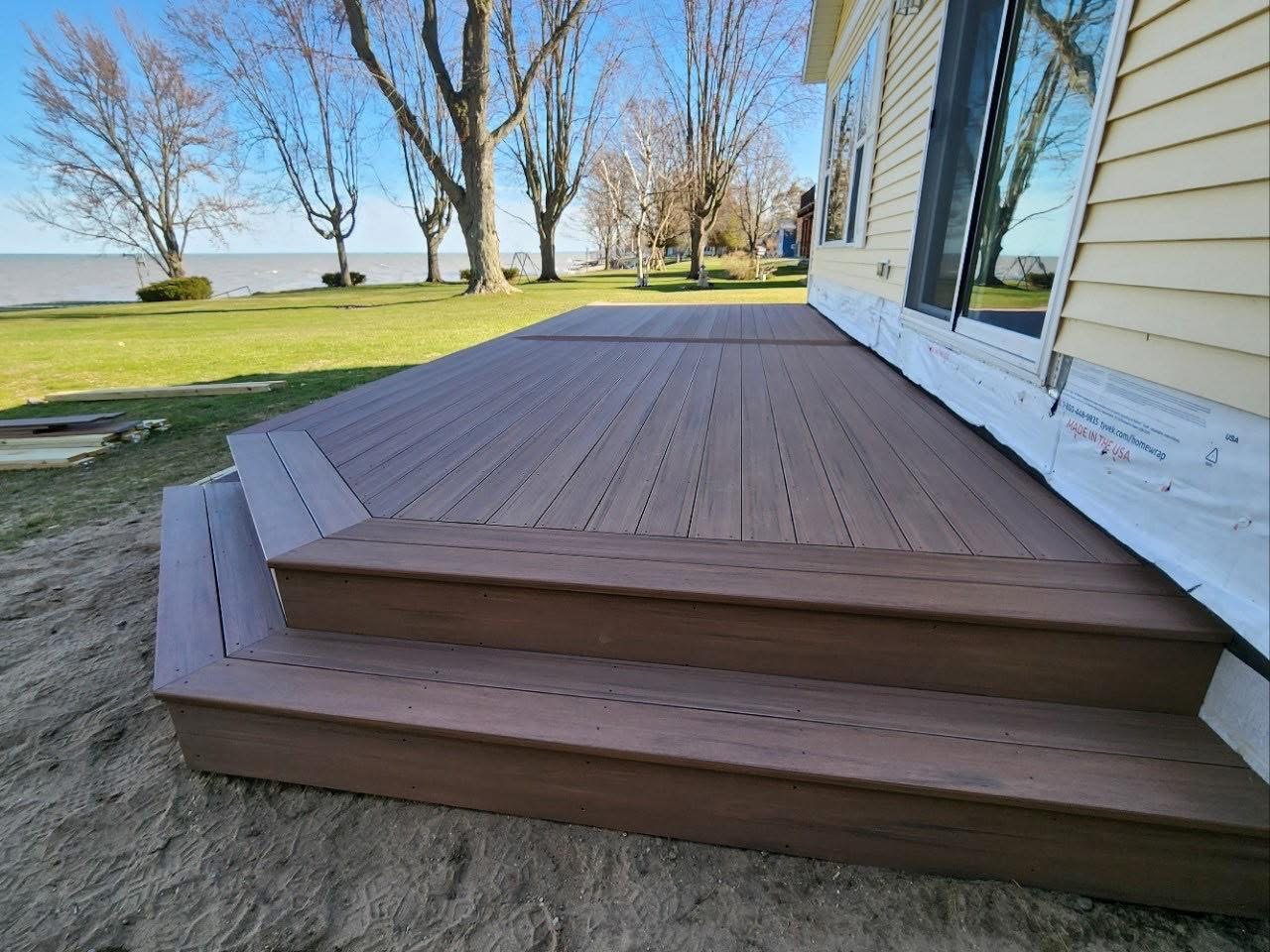 Brown composite deck with wraparound steps beside a lakefront home, deck resurfacing vs replacement in Michigan by Union Properties
