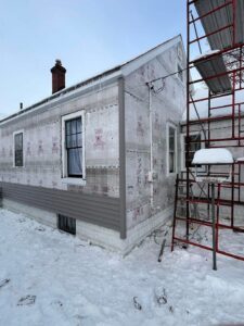 gray vinyl siding panels partially installed over tyvek wrap with scaffold and snow on ground in Port Huron