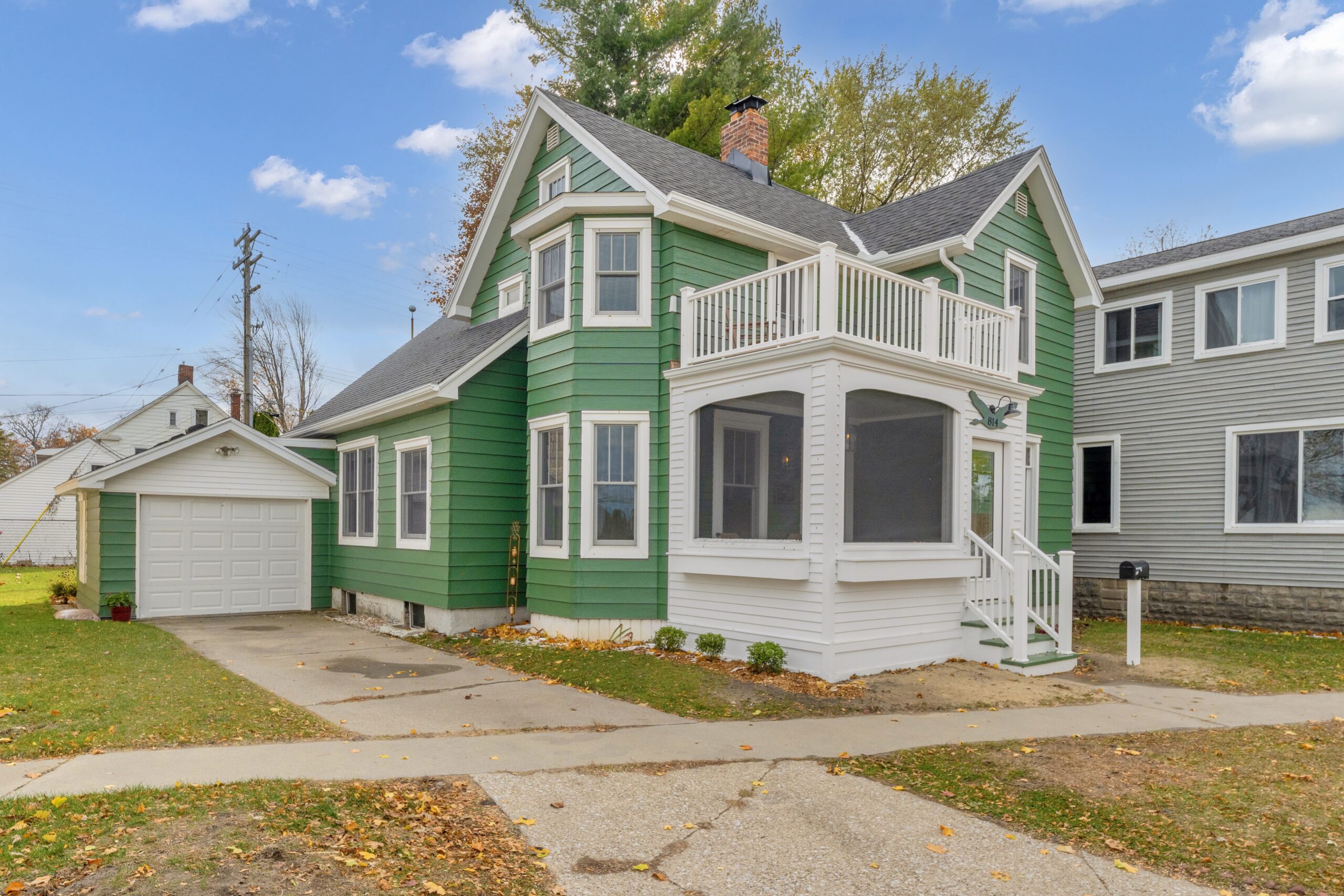 A renovated two-story green siding house with a white screened-in porch, upper balcony, and detached garage, highlighting a historic home remodel Port Huron MI by Union Properties.