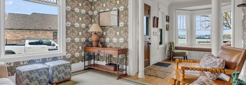 A beautifully remodeled living room featuring intricate vintage floral wallpaper, a stained glass window, and classic wooden columns, showcasing a historic home remodel Port Huron MI by Union Properties.