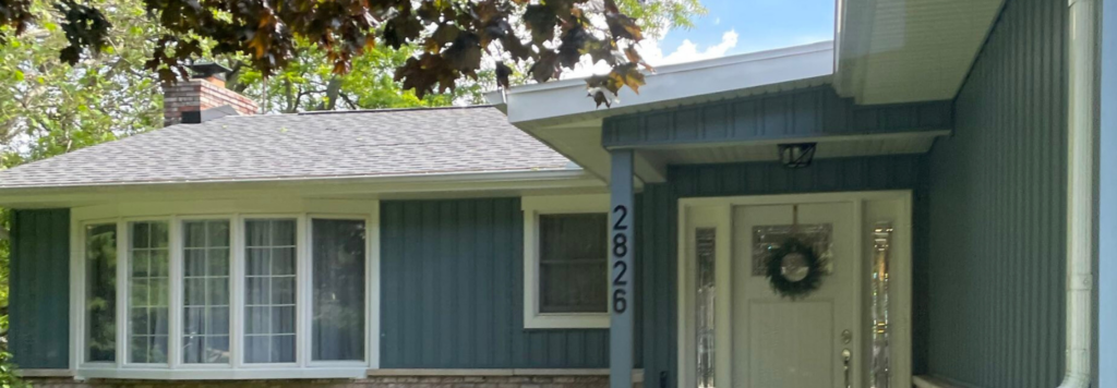 A mid-century ranch home featuring updated blue vertical siding, brick accents, and a concrete walkway, completed by a local siding contractor Port Huron in Port Huron by Union Properties.