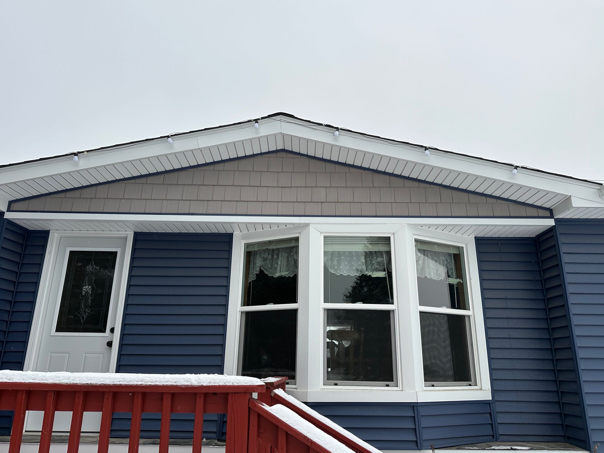 A large three-panel bay window with bright white vinyl trim on a dark blue home exterior featuring custom window installation and replacement in Port Huron by Union Properties.