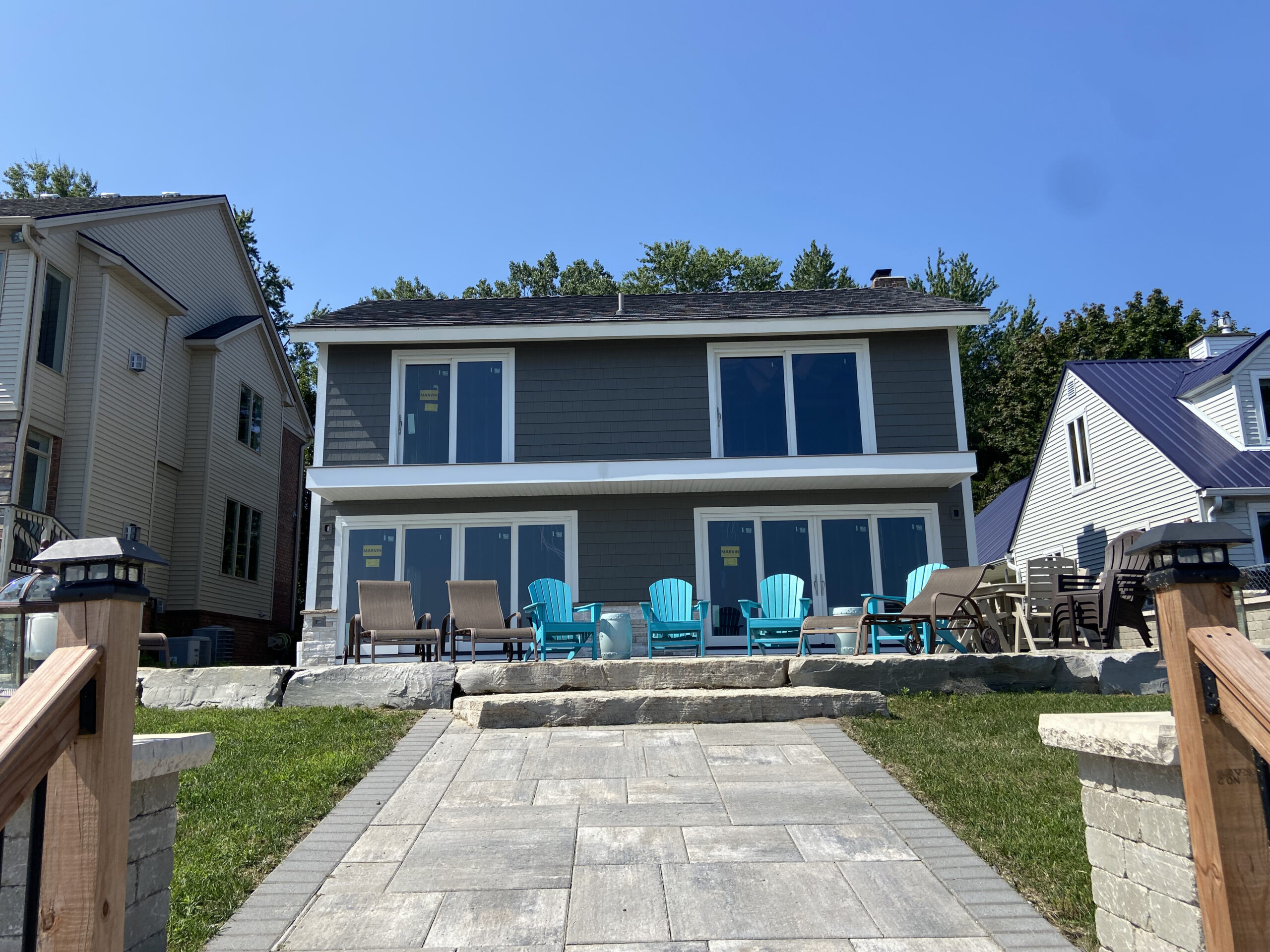 A two-story waterfront home with dark gray siding, large sliding glass doors, and expansive patio windows highlighting window installation and replacement in Port Huron by Union Properties.